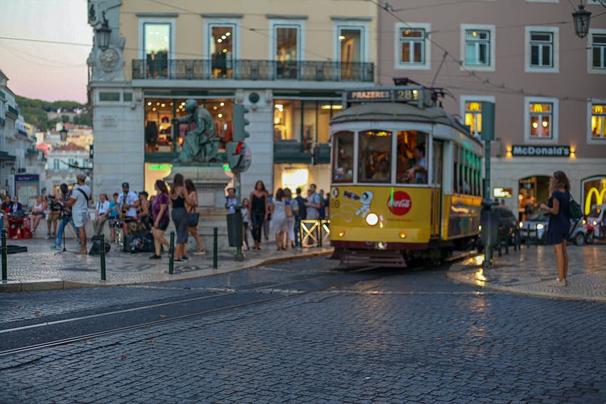 A yellow tram in an area busy with pedestrians at dusk 