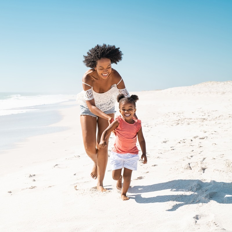 Young Mother Looking Happy As She Strolls Down The Beach With Her Daughter Or Young Child, Caribbean Beach